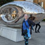 Author Carol Van Natta standing in front of a shiny sculpture in the courtyard of the Museum of Modern Art in Sydney, Australia